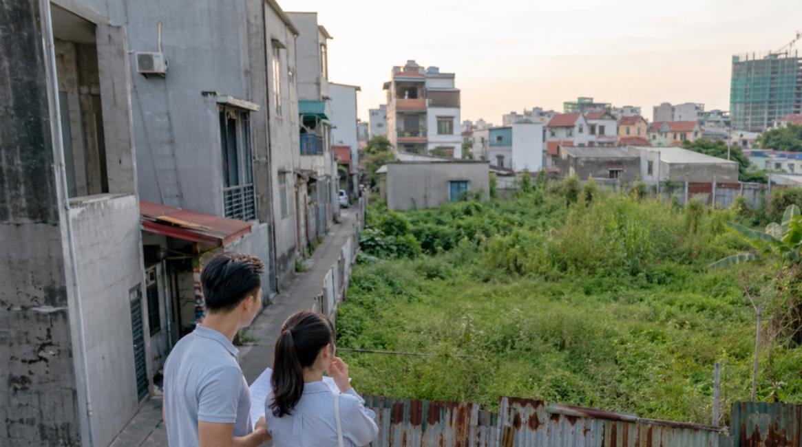 Đất xen kẹt không sổ đỏ nằm giữa khu dân cư, cặp vợ chồng trẻ đứng xem đất